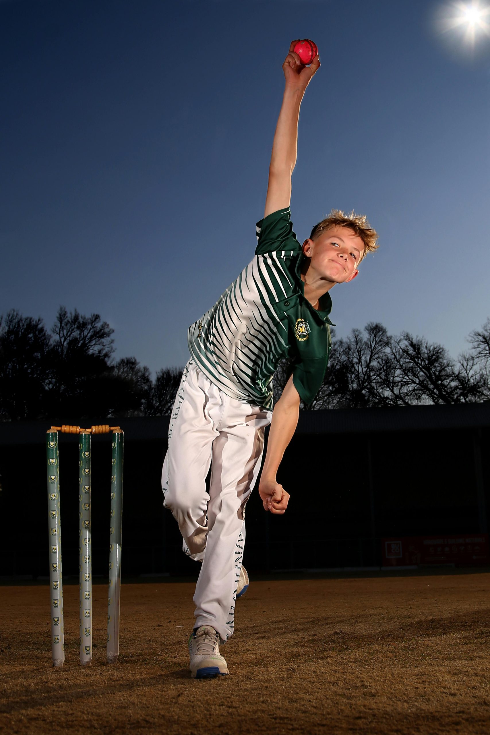 Cricket fast bowler delivering a powerful throw during dusk at a stadium.